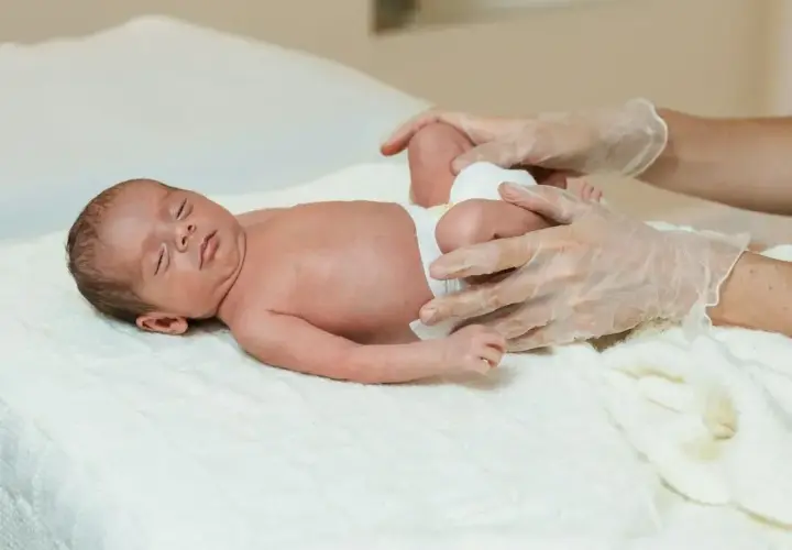 Delikatne badanie niemowlaka, ocena symetrii kończyn. Ręce w rękawiczkach badają nóżki maluszka.