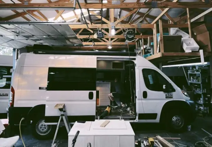 Aménagement d'un camion en cours dans un garage. Un homme travaille à l'intérieur, entouré d'outils et de matériaux.