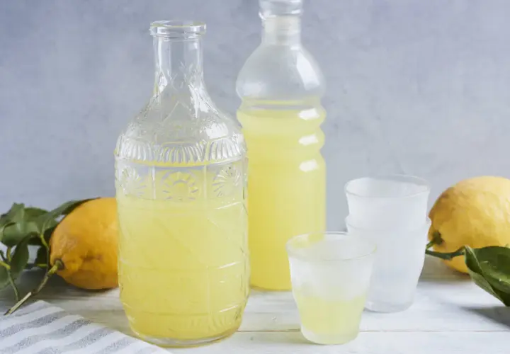 Ein Glas mit dem original italienischen Limoncello Rezept, daneben eine Karaffe, Flasche und Zitronen.