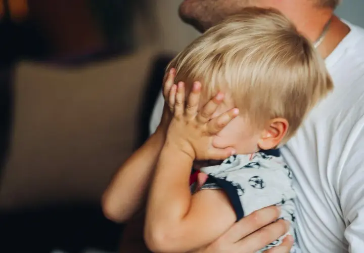 20 miesięczne dziecko budzi się w nocy, ukrywając twarz w dłoniach. Tata tuli go, próbując uspokoić.