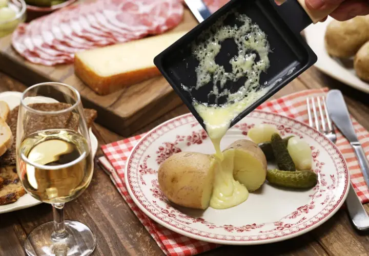 Un accord plat vin parfait : raclette fondue sur pommes de terre, cornichons, charcuterie et pain, avec un verre de vin blanc.