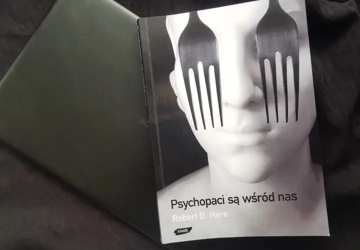 Okładka książki "Psychopaci są wśród nas" z widelcami zamiast oczu na twarzy.