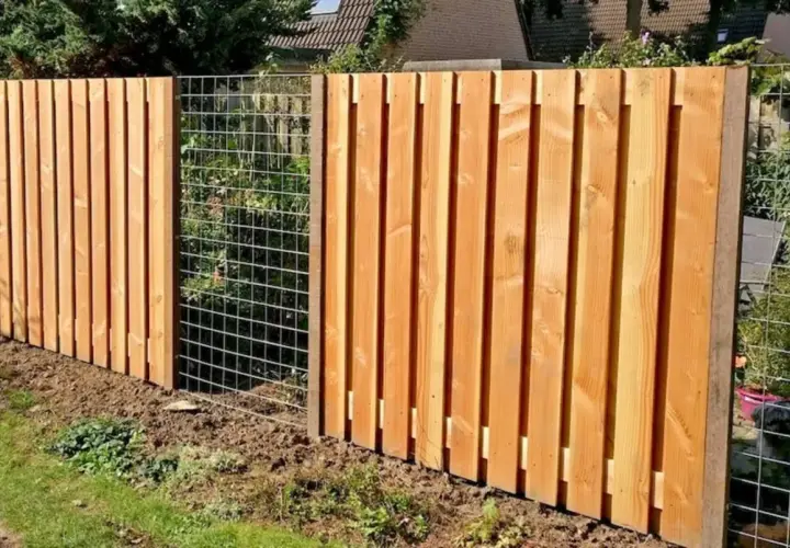 Clôture en bois reconstitué, avec des planches verticales et une section grillagée. Un chien est visible derrière le grillage.