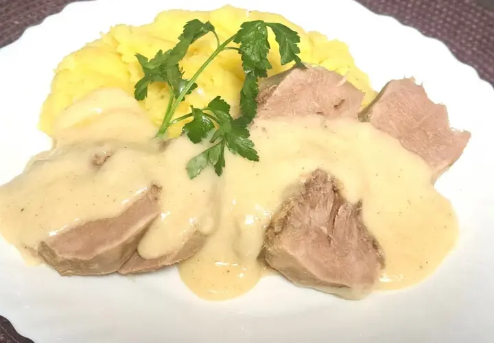 Kawałki ozorków w kremowym sosie chrzanowym, podane z purée ziemniaczanym i gałązką natki pietruszki.