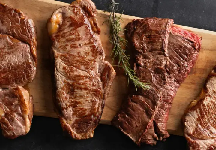 Quatre types de viande rouge grillée, dont un côte de bœuf, sont présentés sur une planche en bois.