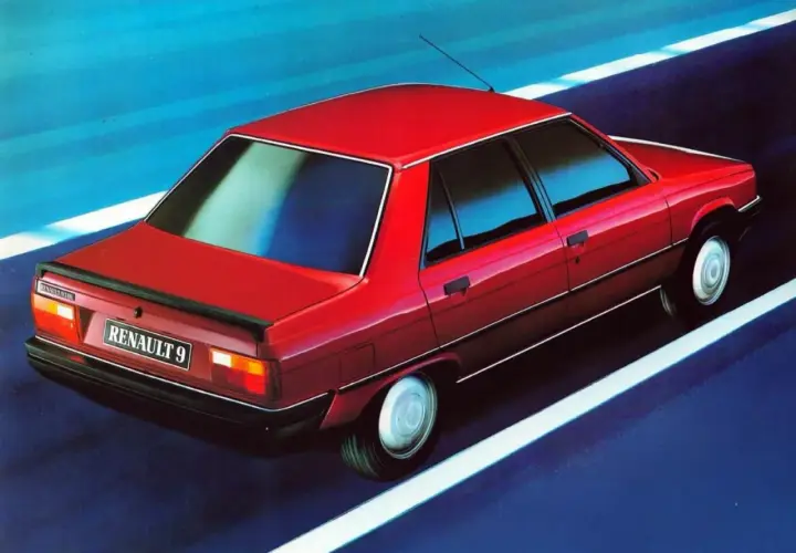 Czerwony Renault 9 sunie po drodze, odbijając niebieskie niebo w szybach.