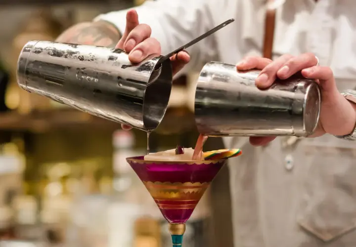 Barman przelewa drinka z shakera do drinków do ozdobnego kieliszka.