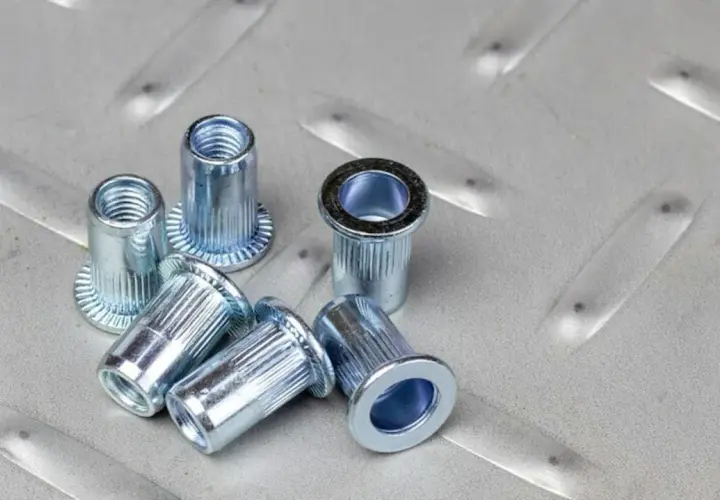 Kilka metalowych nitotrzpieni leży na chropowatej, metalowej powierzchni.