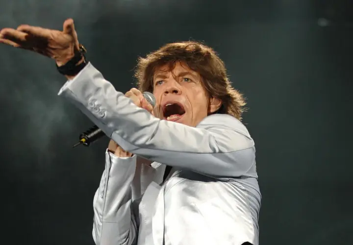 Mick Jagger, wokalista zespołu, śpiewa z mikrofonem, gestykulując ręką.
