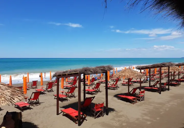Plage de Marina di Bibbona avec des chaises longues rouges et des parasols de paille sous un ciel bleu éclatant.
