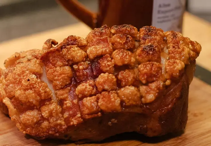 Ein knuspriger, ofenfrischer Schweinebraten mit goldbrauner Kruste liegt auf einem Holzbrett.
