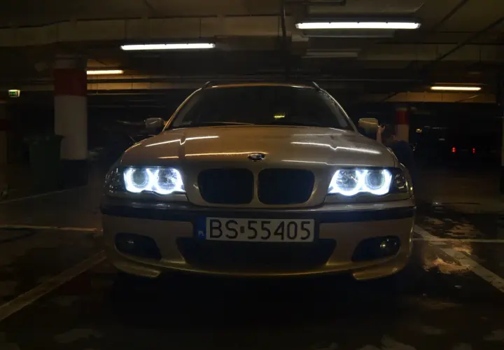 Złote BMW E46 z włączonymi ringami świeci w ciemnym garażu.
