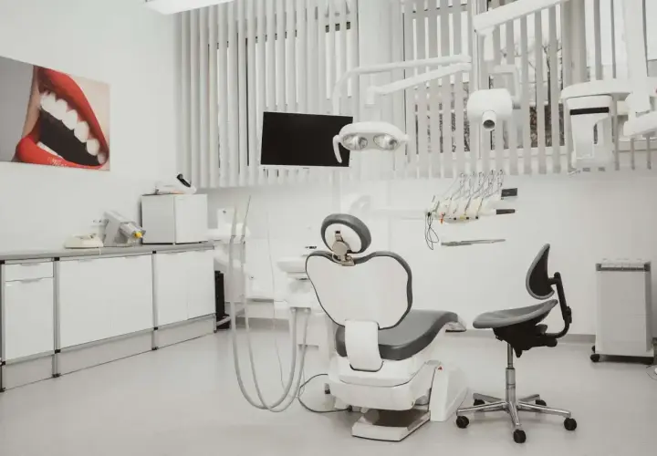 Nowoczesny gabinet stomatologiczny i ortodontyczny. Biały fotel dentystyczny, lampa, wiszące narzędzia i obraz z uśmiechem.