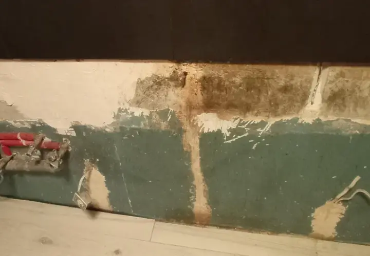 Preparazione per carteggiare muro per imbiancare: tubi rossi e impianto a vista, intonaco scrostato e macchie.