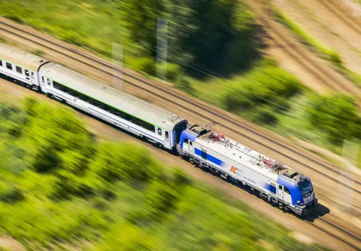 Pociąg PKP Intercity pędzi przez zielone krajobrazy. Szybko kupisz bilet na podróż przez aplikację do zakupu biletów PKP.
