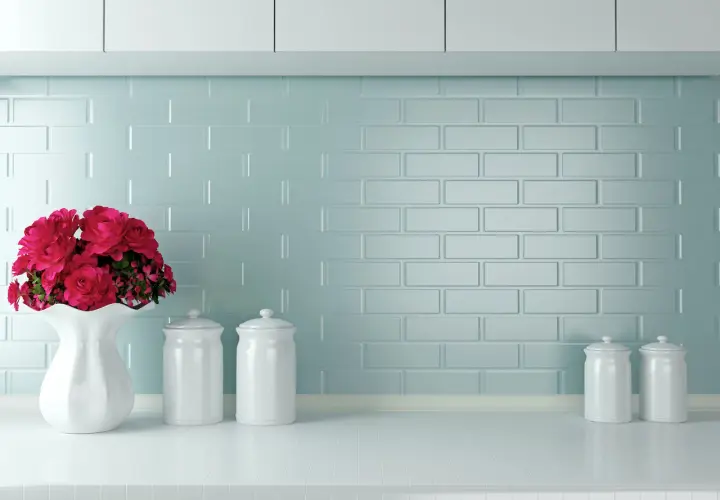 Un mazzo di rose rosse in un vaso bianco su un piano di lavoro, con barattoli bianchi e uno sfondo di piastrelle azzurre. Ottime opinioni per dipingere piastrelle cucina.