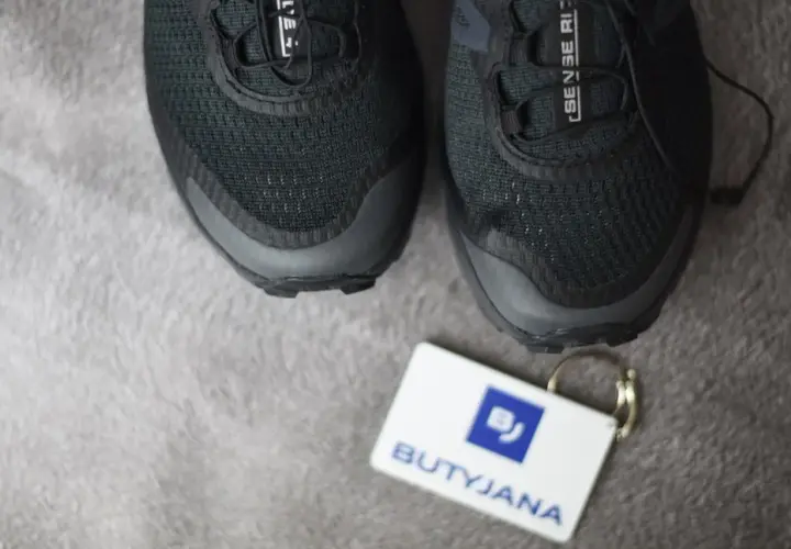 Czarne buty Salomon, model Sense Ride, z metką "BUTYJANA". Salomon to znana firma produkująca odzież i obuwie sportowe.