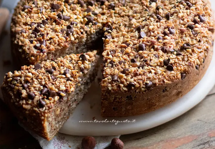 Una deliziosa torta di nocciole, ricoperta di granella di nocciole e gocce di cioccolato, con una fetta tagliata.