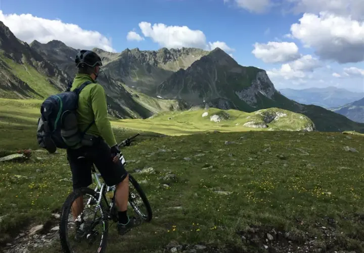 Rowerzysta w zielonej bluzie i kasku z plecakiem na plecach podziwia alpejski krajobraz. Idealny plecak na rower na taką wyprawę.