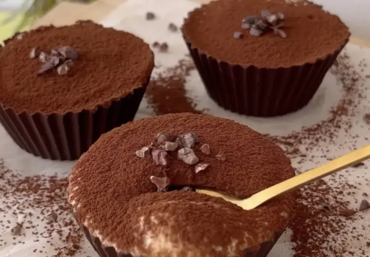 Delicioso postre con ricota, cubierto de cacao y trocitos de chocolate. Una cuchara dorada se hunde en uno de ellos.