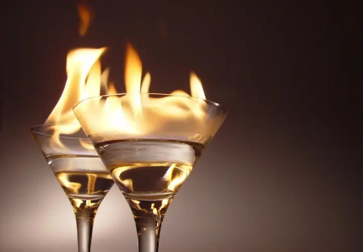 Dwa kieliszki z płonącym alkoholem na ciemnym tle.