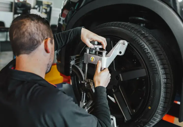 Mecánico ajusta un sensor en la rueda de un coche. Averigua cuanto cuesta alinear un coche para un manejo seguro.