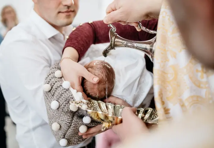 Woda święcona spływa na główkę niemowlęcia, rozpoczynając uroczysty obrzęd chrztu.