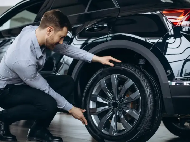 Man inspekterar däcket på en svart bil, redo för ett kumho ecsta ps71 test.