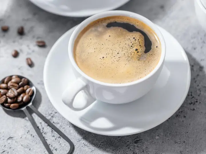 Aromatic coffee in a white cup, with beans on a spoon. Czy kawa jest lekkostrawna? To zależy od sposobu parzenia.