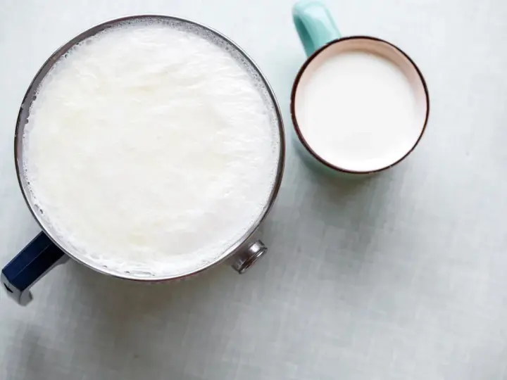 Un pot de lait chaud avec une fine peau de lait à la surface, à côté d'une tasse remplie de lait frais.