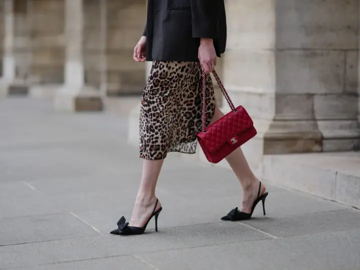 Elegancka kobieta w sukience w panterkę i czarnym blazerze, z czerwoną torebką Chanel. Czy sukienka w panterkę jest modna? Zdecydowanie tak!