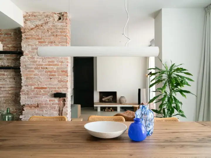 Salón con pared de ladrillo visto, mesa de madera con jarrones y planta.