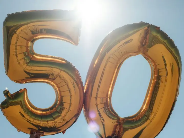 Gyllene ballonger formar siffran 50 mot en klarblå himmel. Perfekt för roliga frågor till 50 års fest!