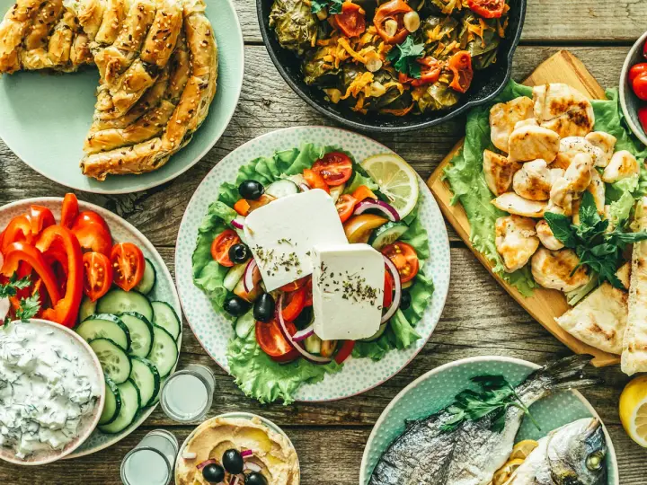 Pyszny grecki posiłek: pieczona ryba, sałatka grecka, kurczak, hummus i ciasto filo, które ma dużo węglowodanów.