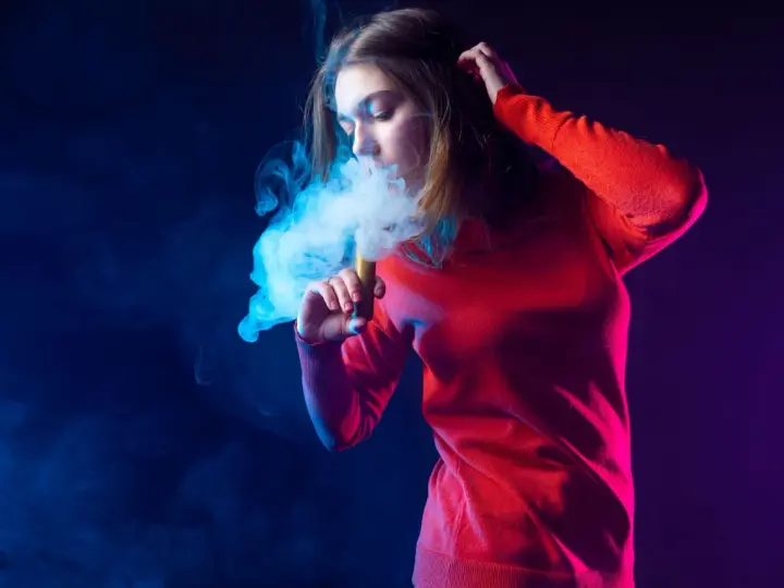 Joven exhala humo azul de un vaper. El vaper con nicotina es malo para la salud.