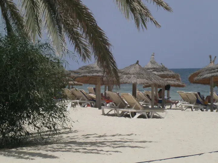 Plaża na Djerbie z leżakami i parasolami. Ludzie odpoczywają, co sugeruje, że na Djerbie jest bezpiecznie.
