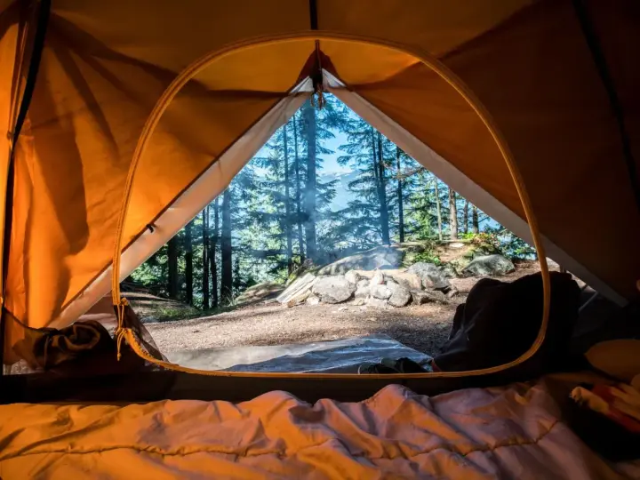 Vue de l'intérieur d'une tente orange, un feu crépite dehors. L'obligation sécurité camping est respectée avec ce campement bien installé.