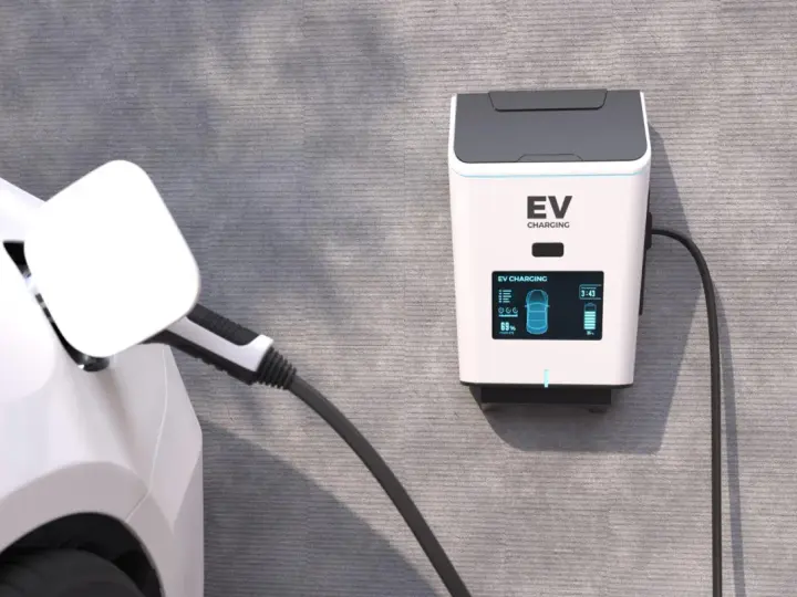 Biały samochód elektryczny podłączony do ładowarki EV na ścianie.