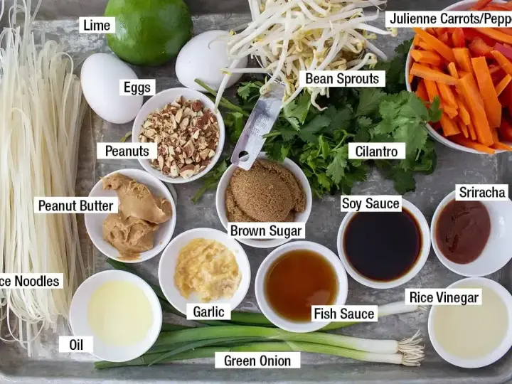 Składniki do sosu pad thai: makaron ryżowy, jajka, orzeszki ziemne, masło orzechowe, olej, czosnek, zielona cebulka, brązowy cukier, kiełki fasoli, kolendra, marchewka, papryka, sos sojowy, sos rybny, ocet ryżowy, sriracha, limonka.