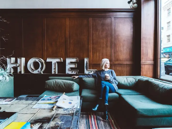 Kobieta z kawą siedzi na kanapie w hotelu. Zastanawia się, ile zarabia technik hotelarstwa.
