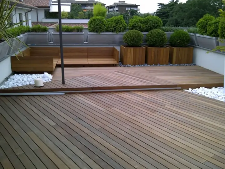 Un balcone trasformato con un pavimento in legno fai da te, circondato da piante e arredi moderni.