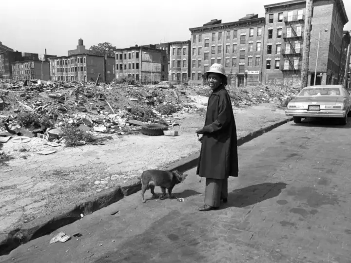 Une femme et son chien devant des immeubles délabrés et des décombres.