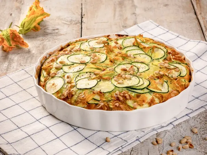 Frittata di zucchine al forno, guarnita con pinoli e fiori di zucca, pronta per essere gustata.