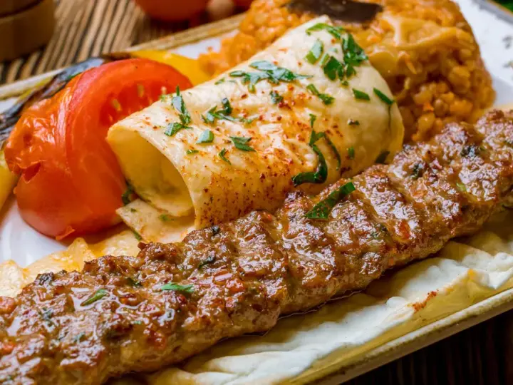 Kebab z mięsa mielonego, grillowane warzywa, placek i ryż na talerzu.