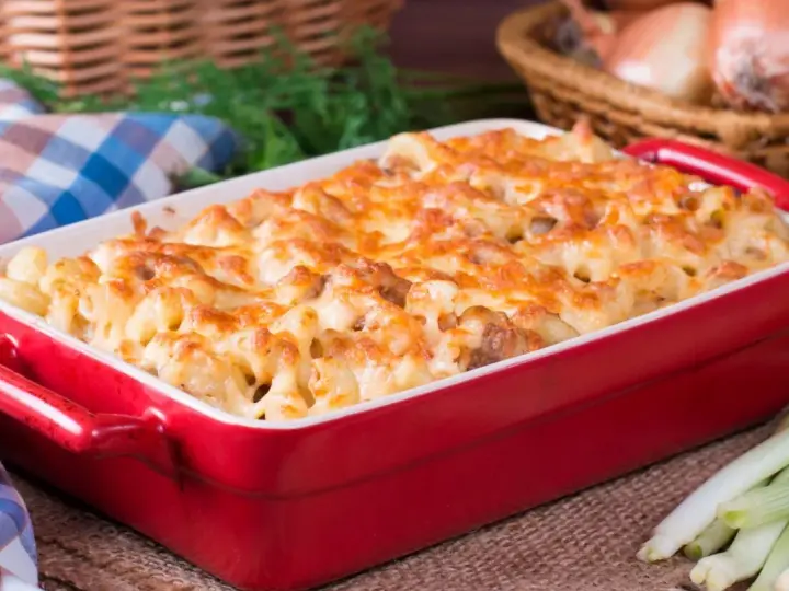 Zapiekanka makaronowa z kurczakiem w czerwonym naczyniu, posypana roztopionym serem.