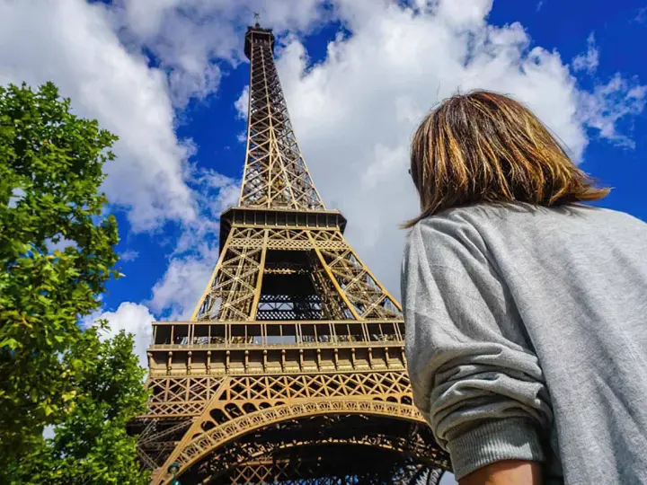 Persona admira la imponente Torre Eiffel bajo un cielo azul con nubes.