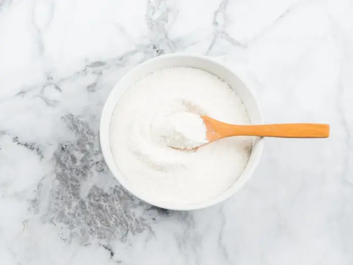 Schüssel mit weißem Pulver, das Kollagenpeptide enthält. Die Wirkung von Kollagenpeptiden ist vielfältig.