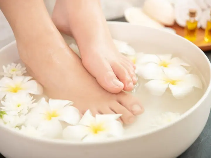 Pies sumergidos en agua con flores blancas, un ritual de spa para probar remedios caseros para quitar el mal olor de los pies.