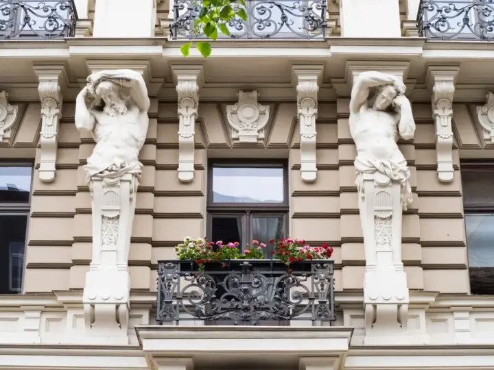 Dwie rzeźby atlantesów podtrzymujące balkon, przykład secesji w sztuce, zdobią fasadę kamienicy.
