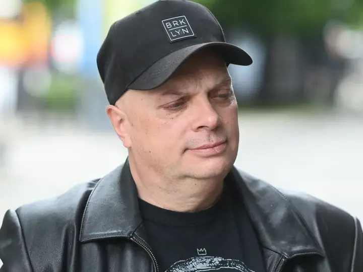 Krzysztof Skiba w czarnej czapce z napisem "BRK LYN" i skórzanej kurtce, zamyślony.